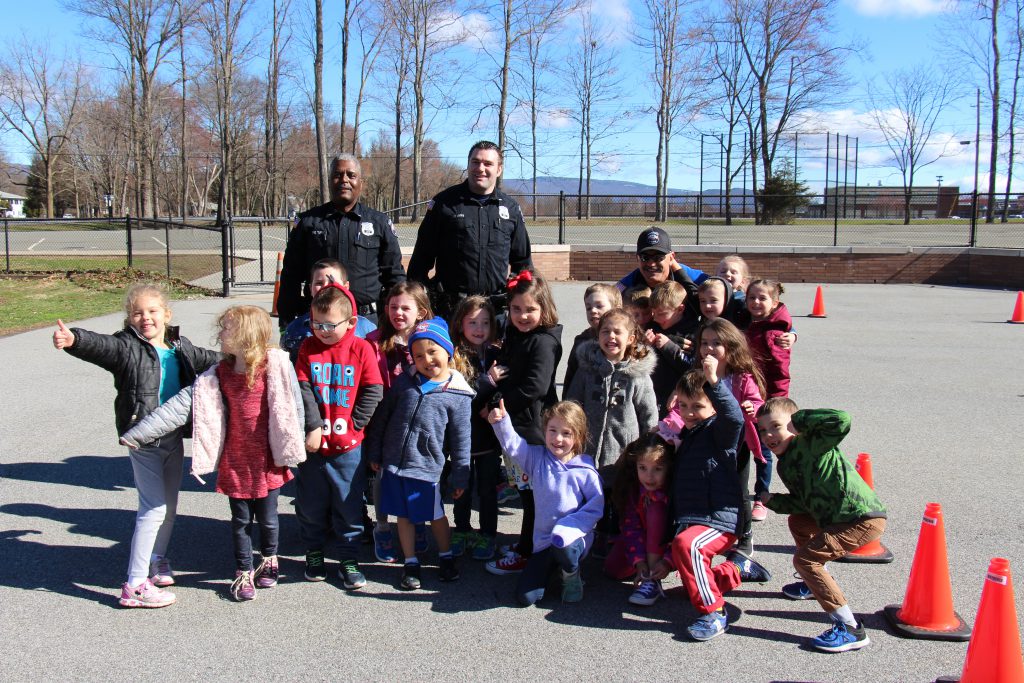 20 kindergarten students smiling with three police officers. Sunny day