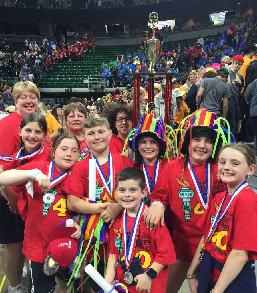 Group of seven elemetary kids wearing red shirts and silver medals along with three adults holding their large trophy