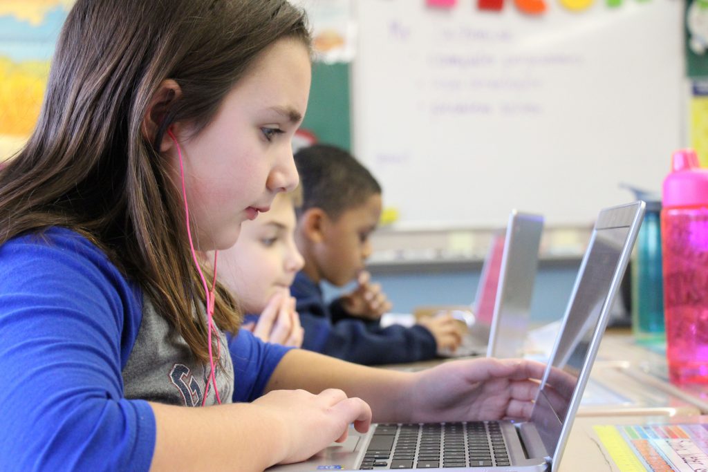 Three elementary students look at their Chromebooks while coding.