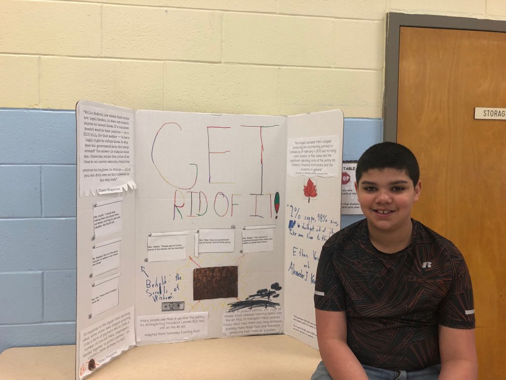 A young boy around 11 years old sits in front of his poster board