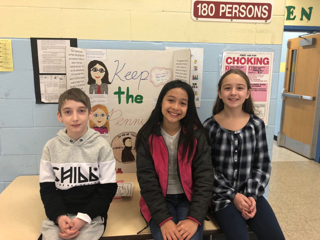 One boy and two girls sit in front of their poster board