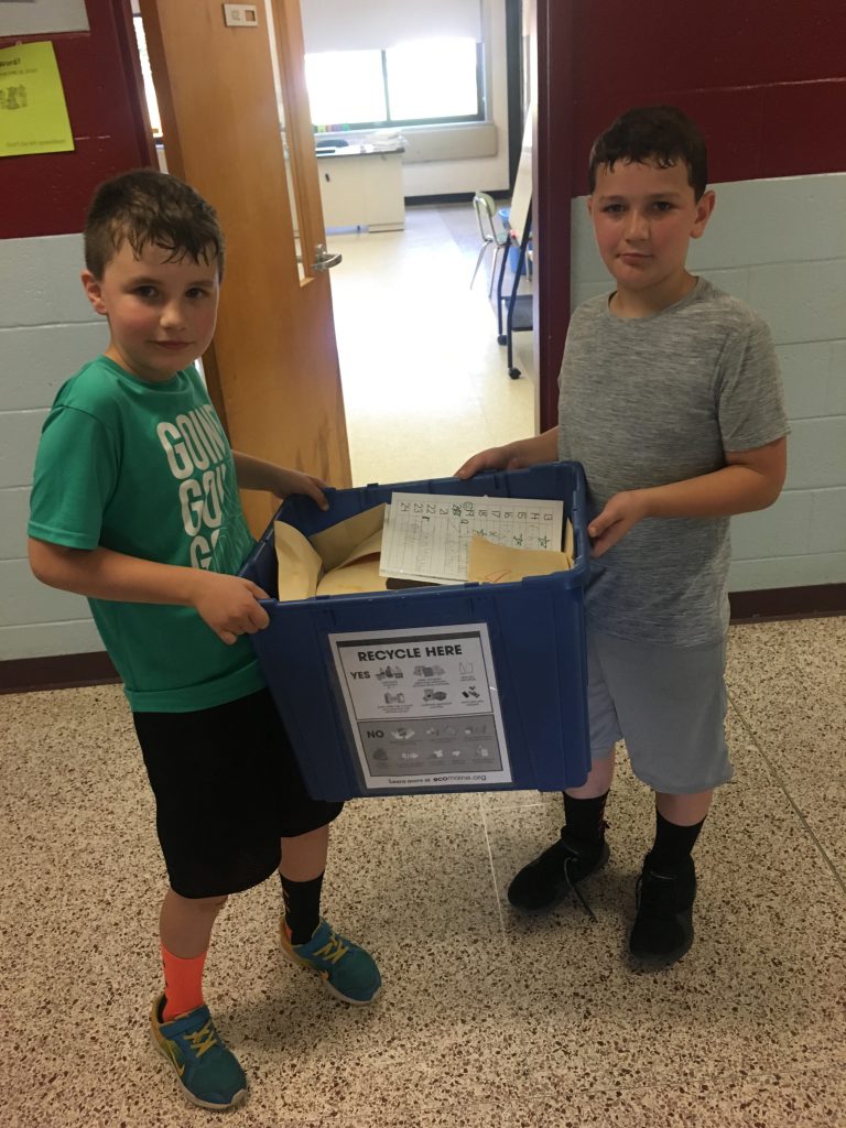 Two boys carry a blue recycle bin.