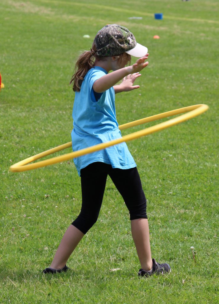 Girl in a light blue t-shirt and baseball cap does the hula hoop