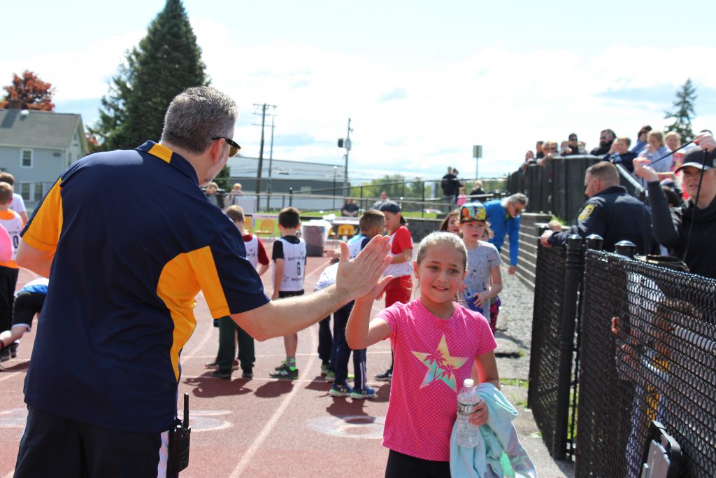 A man wearing a blue and gold shirt high fives a third-grade girl in a pink shirt on the track