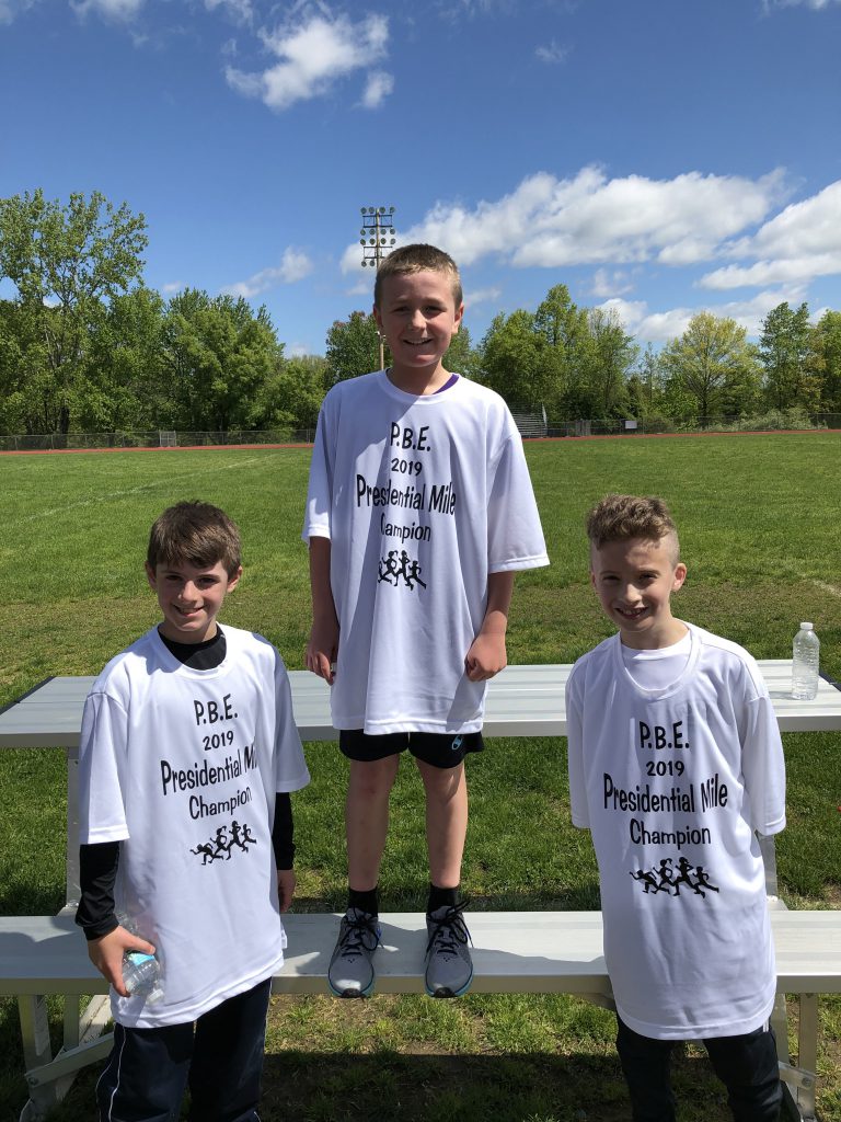 Three fifth-grade boys wearing white t shirts.. First place winner stands in the center.