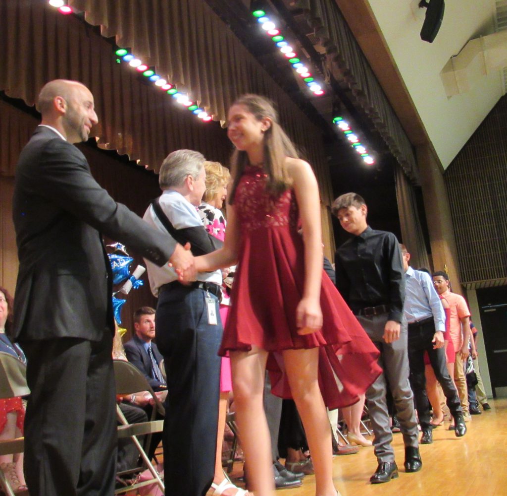 Several young men and women walk across a stage shaking hands with admiistrators