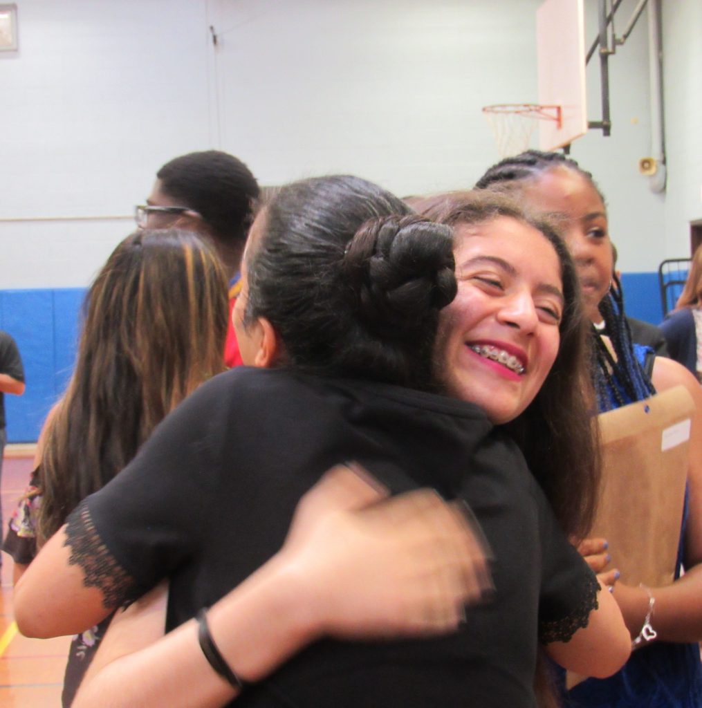 A young woman hugs a woman wearing a dark shirt