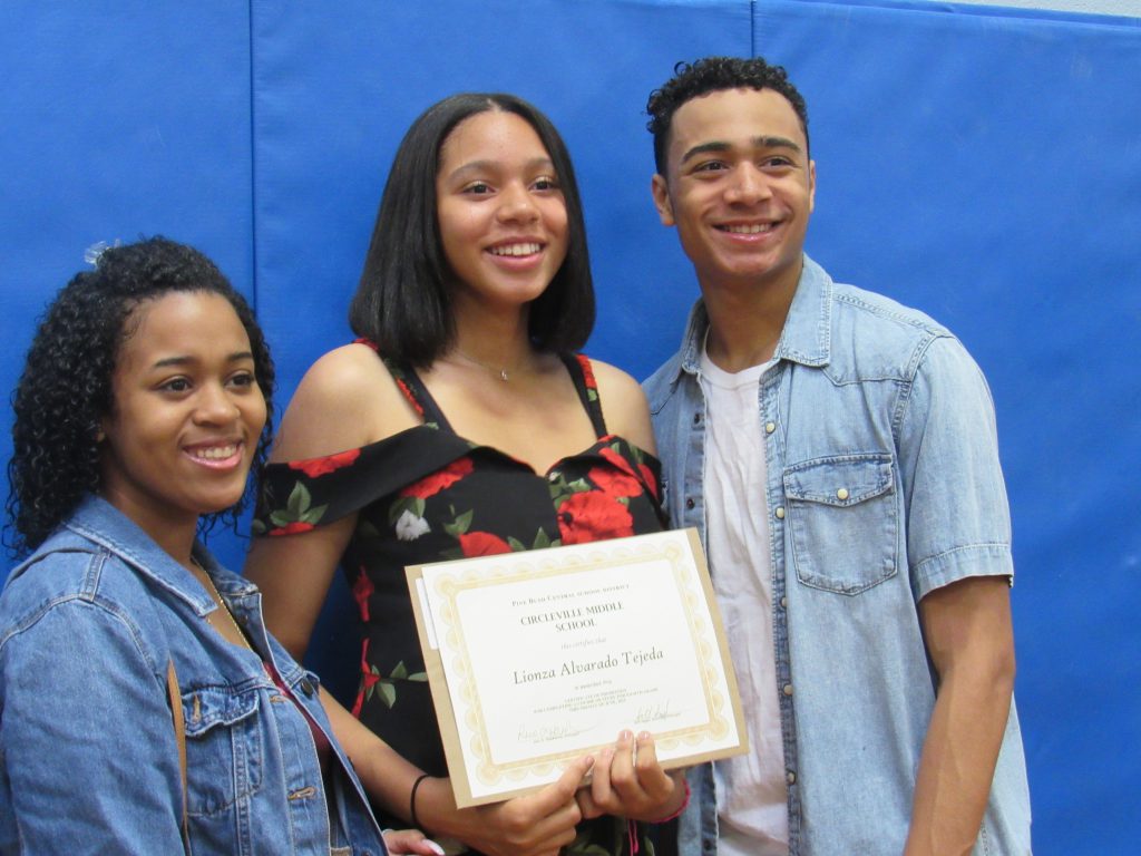 A young woman wearing a black and red dress holds her certificate while flanked by a man and woman.