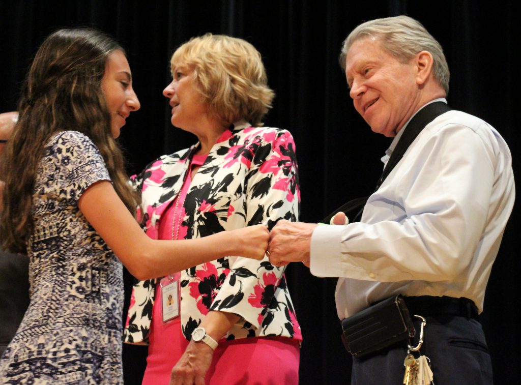 A young woman in a black and white dress fist bumps a man in a white shirt wearing a sling around his other arm