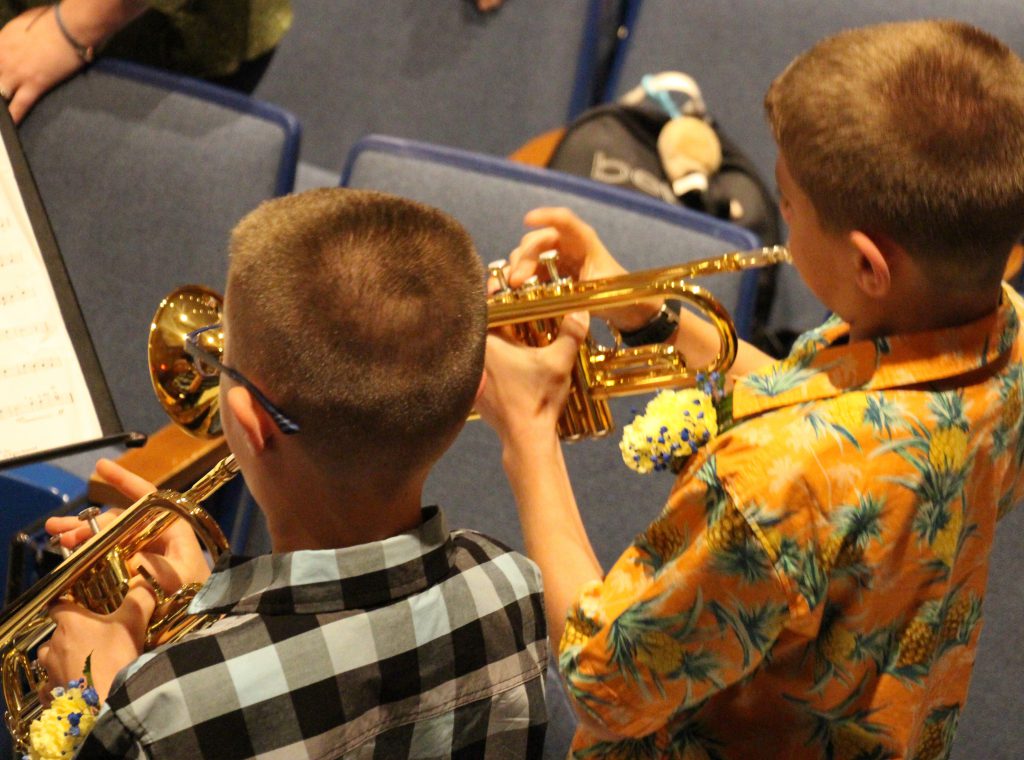 looking over the shoulders of two young men playing horns
