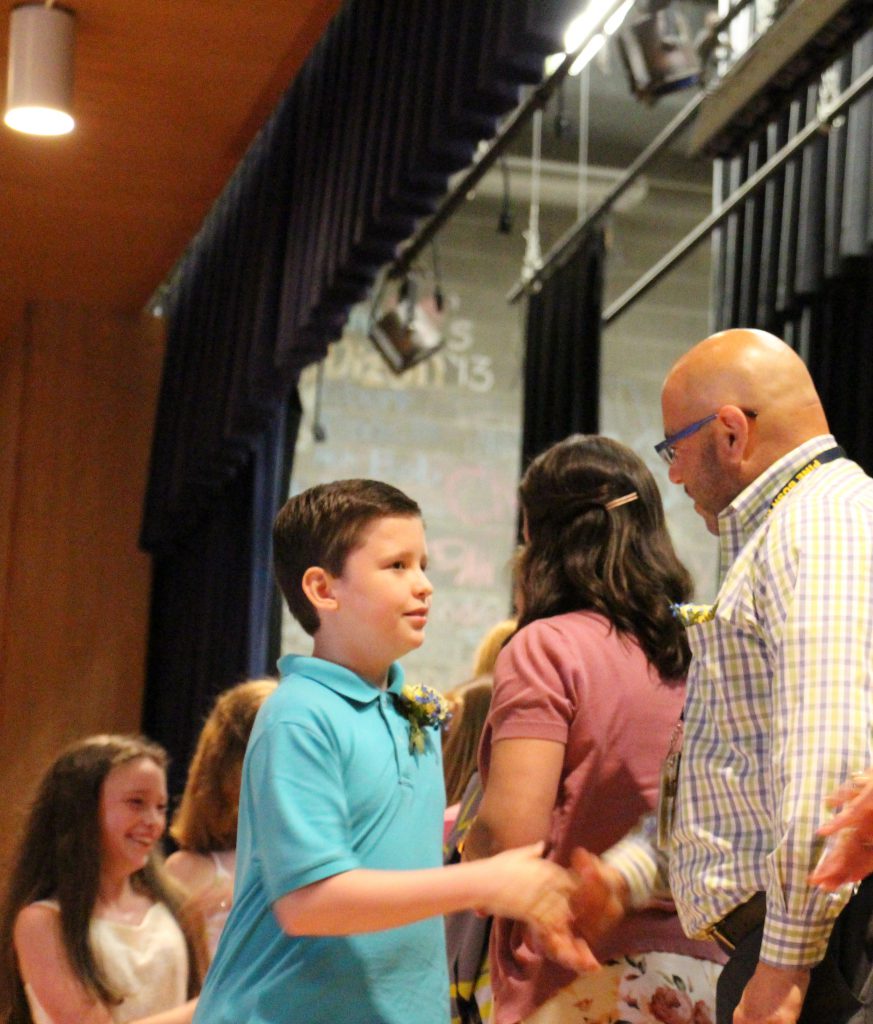 A young man in an aqua colored polo shirt shakes hands with a man in a plaid button down shirt and glasses. 