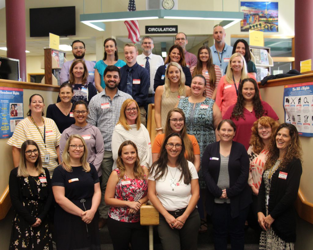 Twenty seven women and men stand in rows on the library stairs smiling