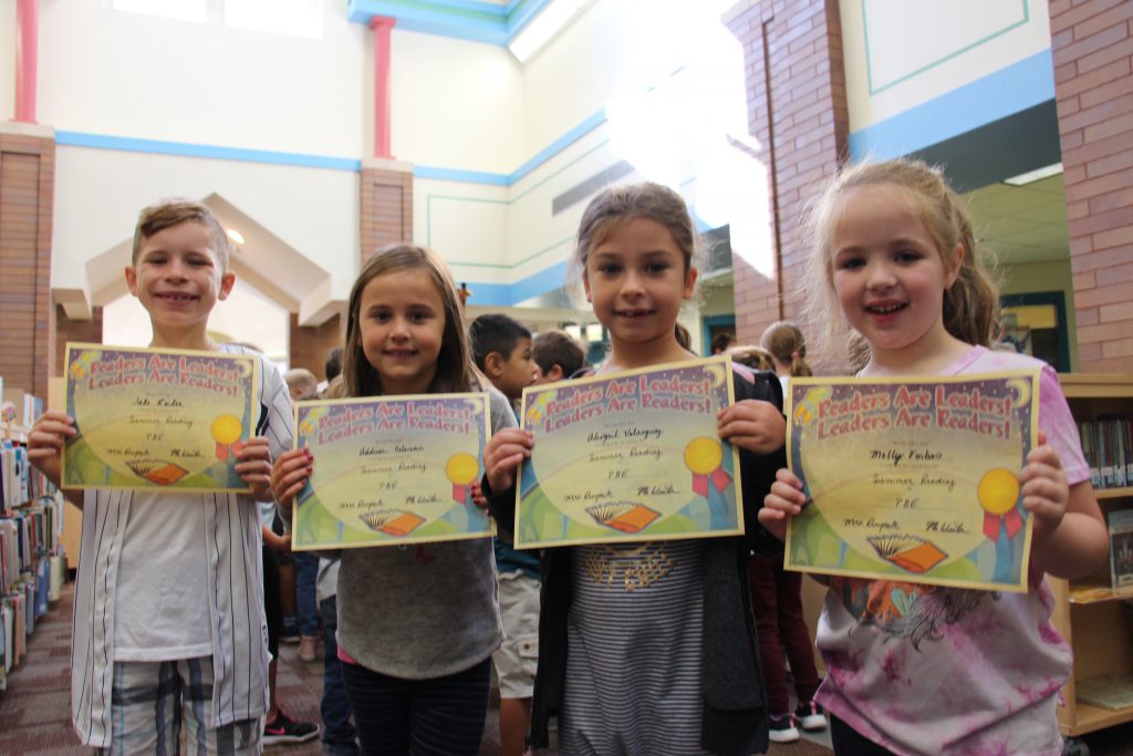 Four elementary students hold up their certificates for reading