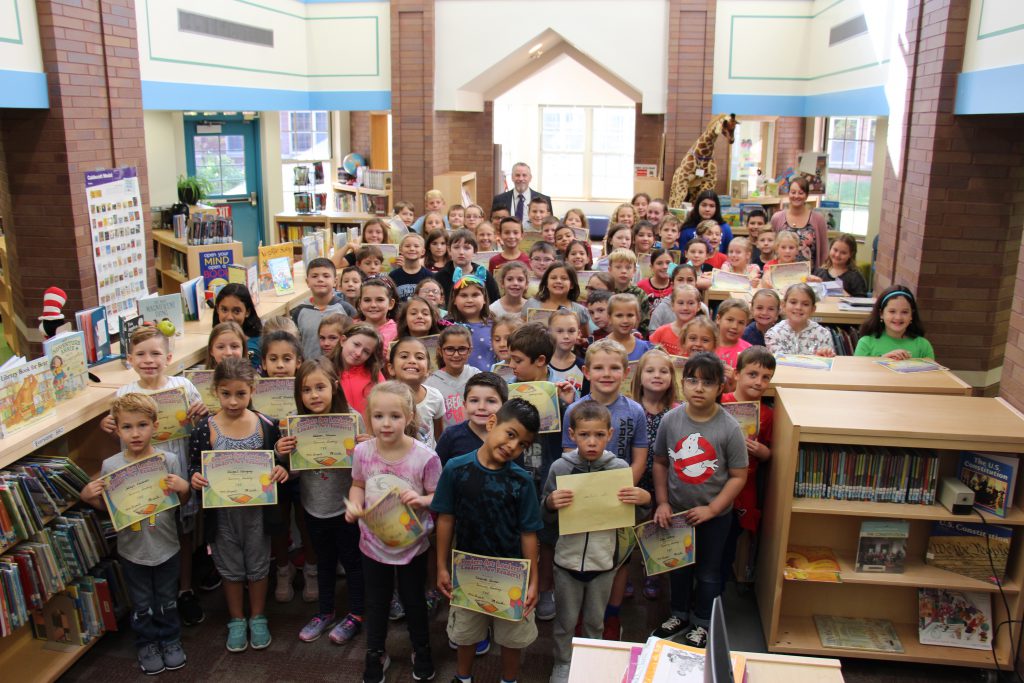Large group of about 80 students pose in the library with their reading certificates. 