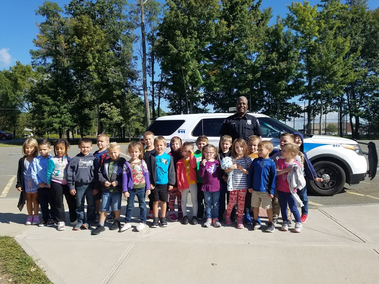 A police officer stands in front of his car with 20 kindergarten students