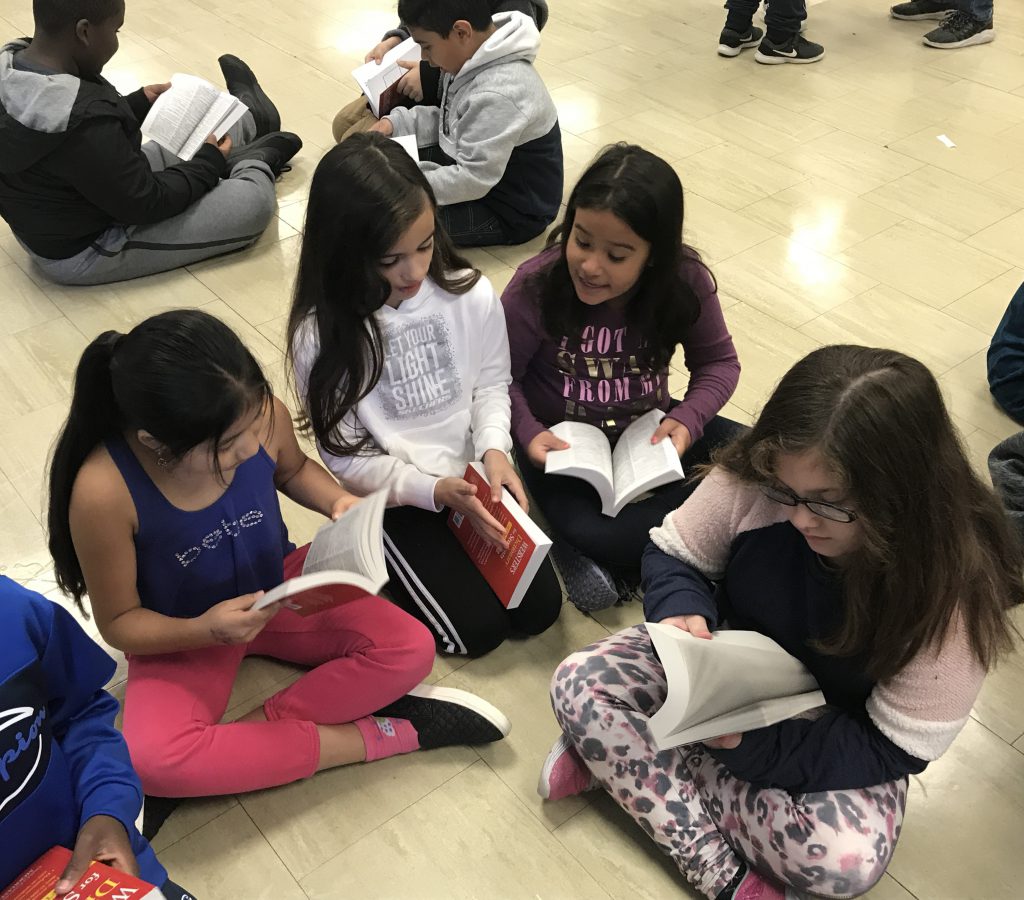 Four girls sitting on the floor go through their new dictionaries.