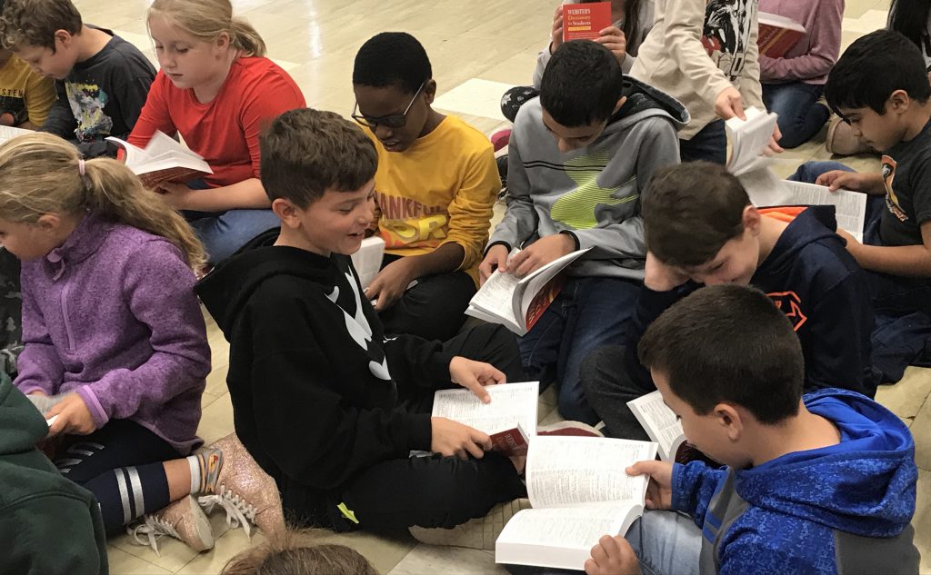 A small group of boys sit on the floor turning the pages of their new dictionaries
