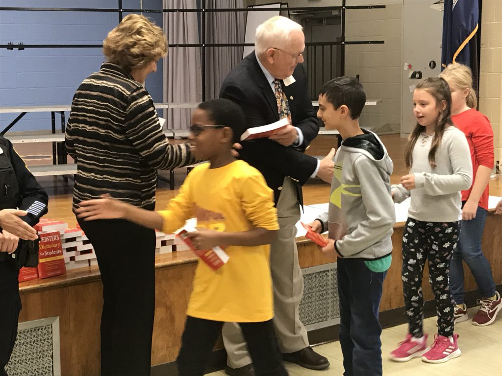 Students shake hands with adults while receiving their new red dictionaries.