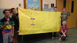 A handful of elementary students hold up a large banner that contains the signatures of family members who signed the No Place for Hate promise.