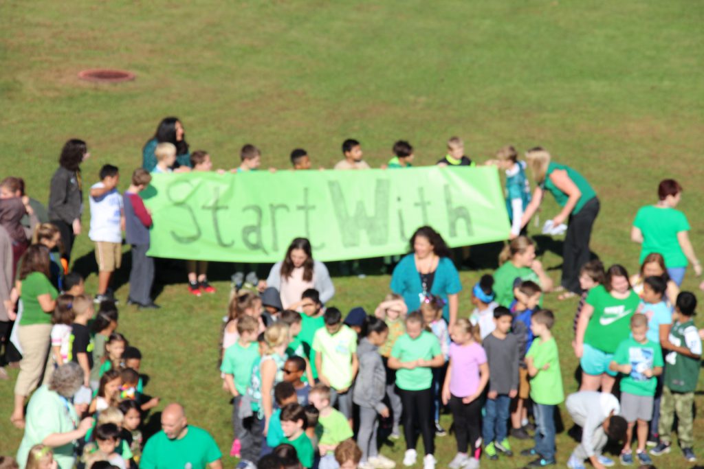 Students hold a green sign that says "Start With" 