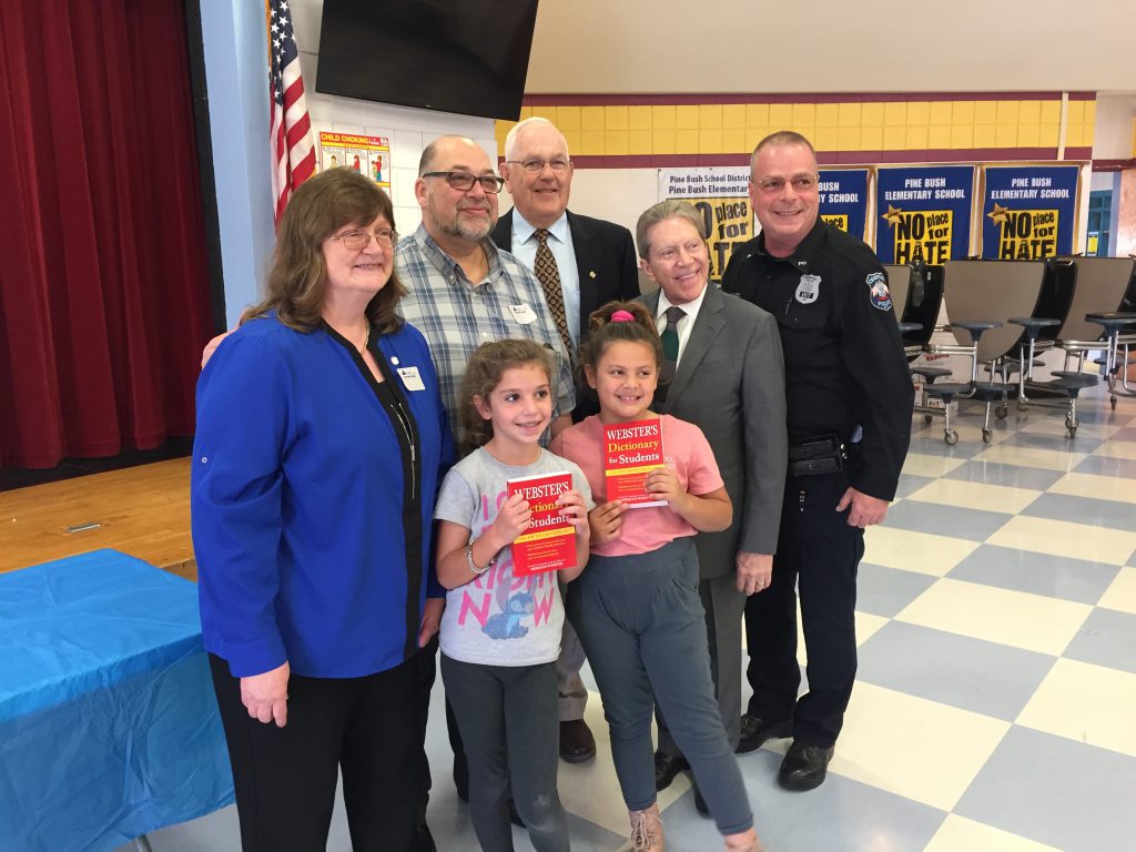 Five adults stand behind two third-grade girls who are holding their new red dictionaries.