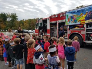 A group of pre-K and kindergarten students listen to a firefighter talk as he shows them different things on the fire engine.