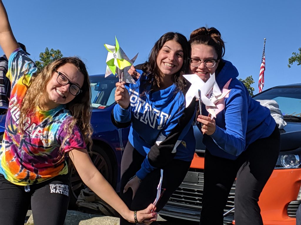 Three high school students smile holding their pinwheels for peace.