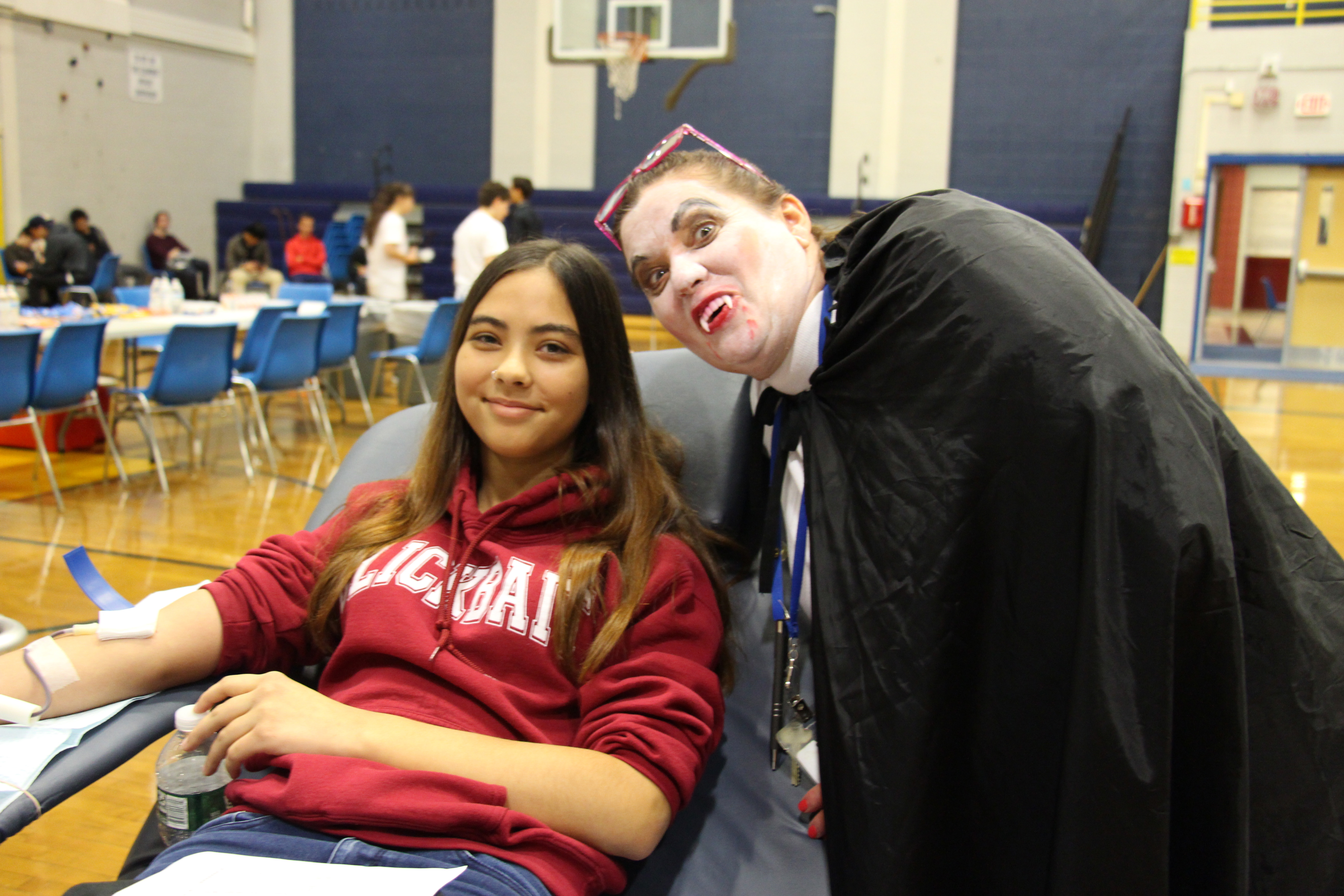 A woman dressed as a vampire stands near a student donating blood.