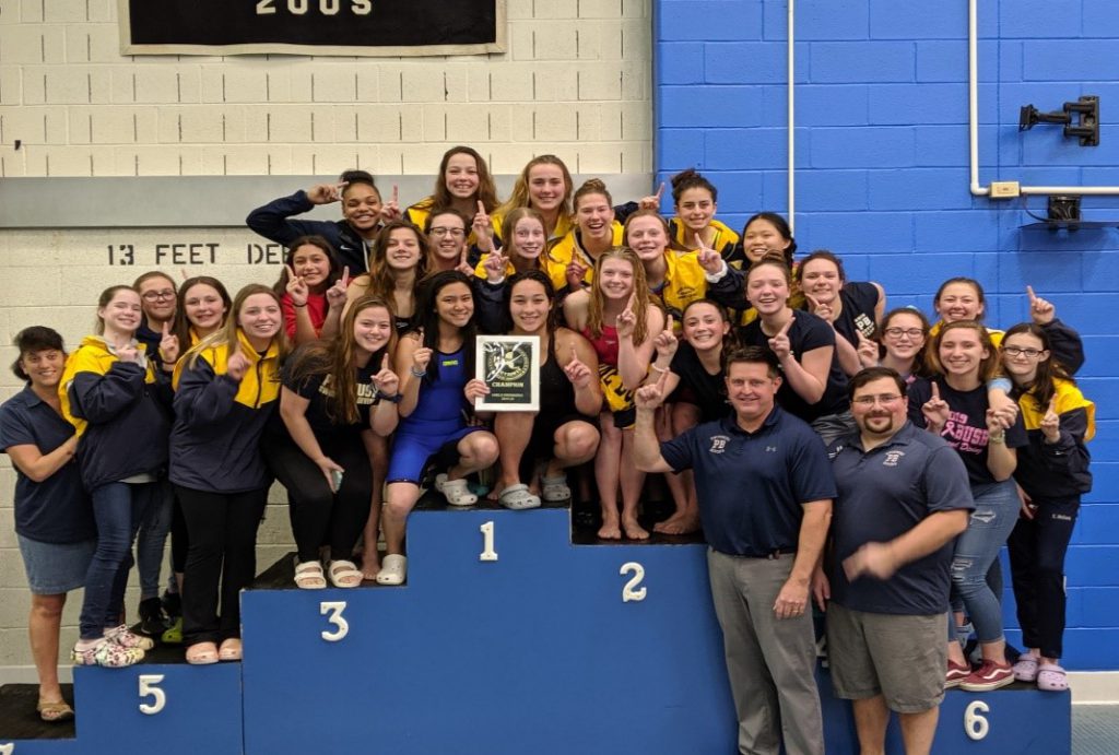 A large group of girls and their coaches are on the podium which has spaces labeled 1, 2 and 3.