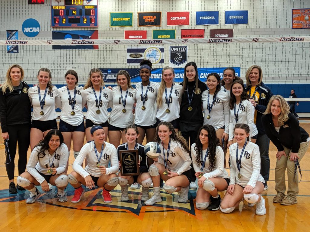 A group of girls with white shirts and medals around their necks pose in two rows, one standing the other kneeling.