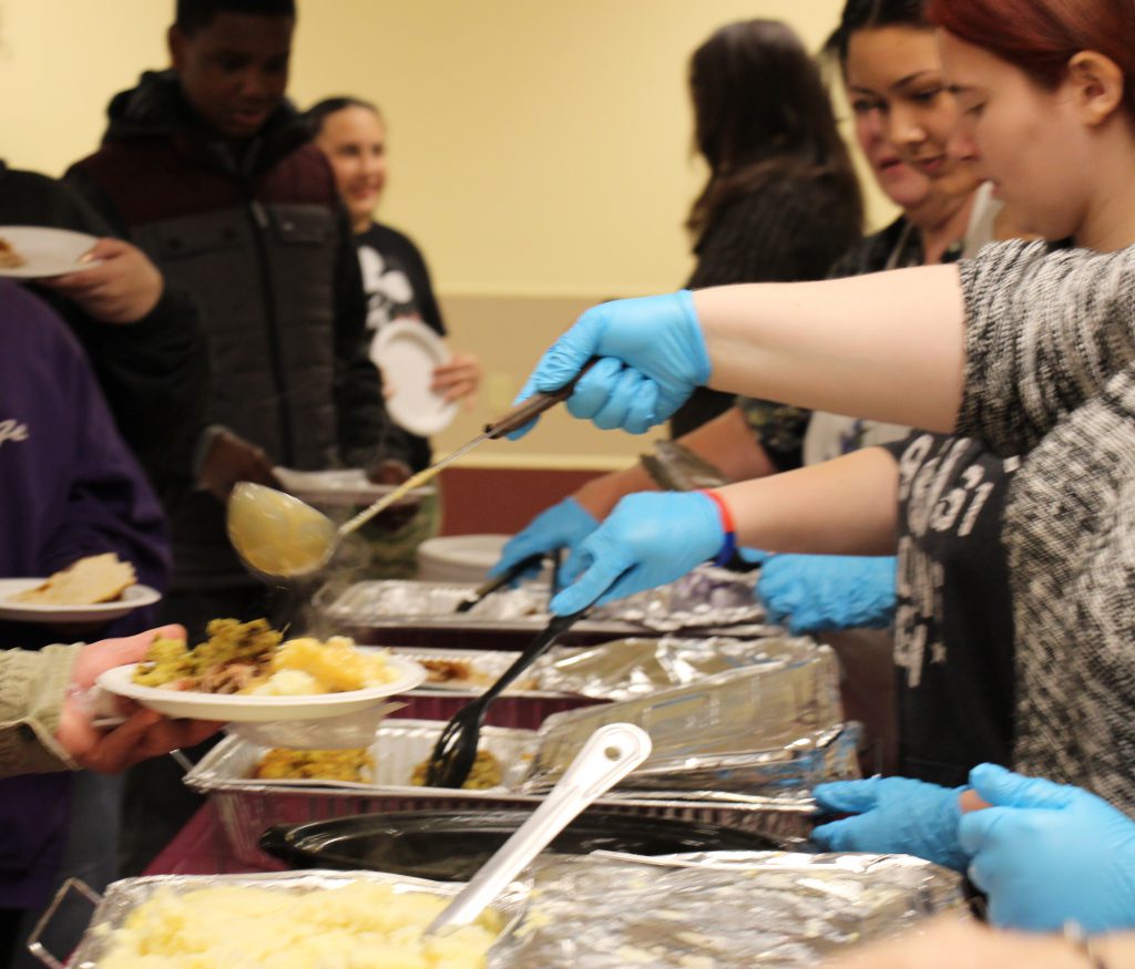 volunteers wearing blue gloves ladle out Thanksgiving food onto plates