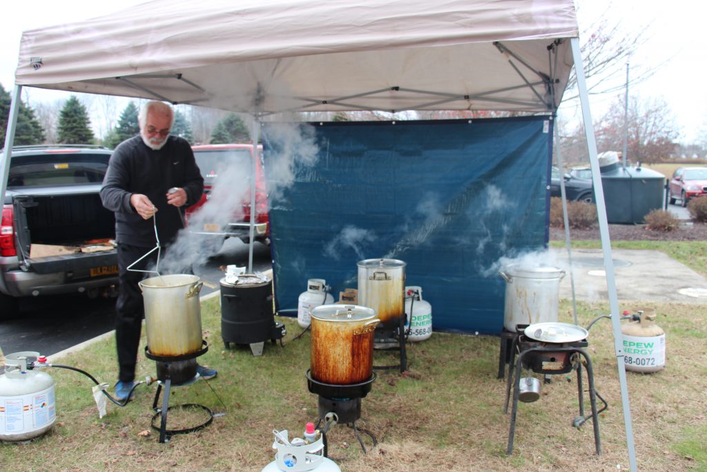 A man holds a handle which is connected to a turkey in a deep fryer. Around him are three other deep fryers with steam coming up.