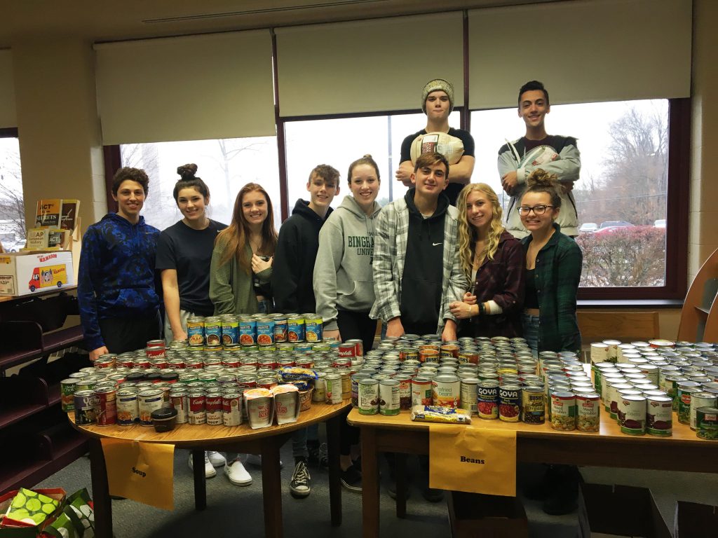 A group of 10 students stand behind two tables filled with canned goods