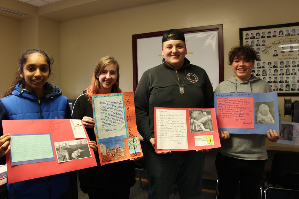 Two high school girls and two high school boys stand holding their art projects