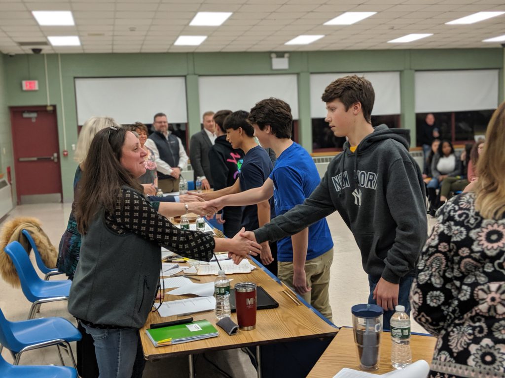 A line of young men shake hands with board of education members