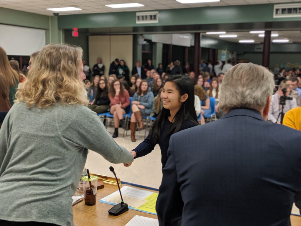 A young woman reaches across a table to shake hands with a woman.