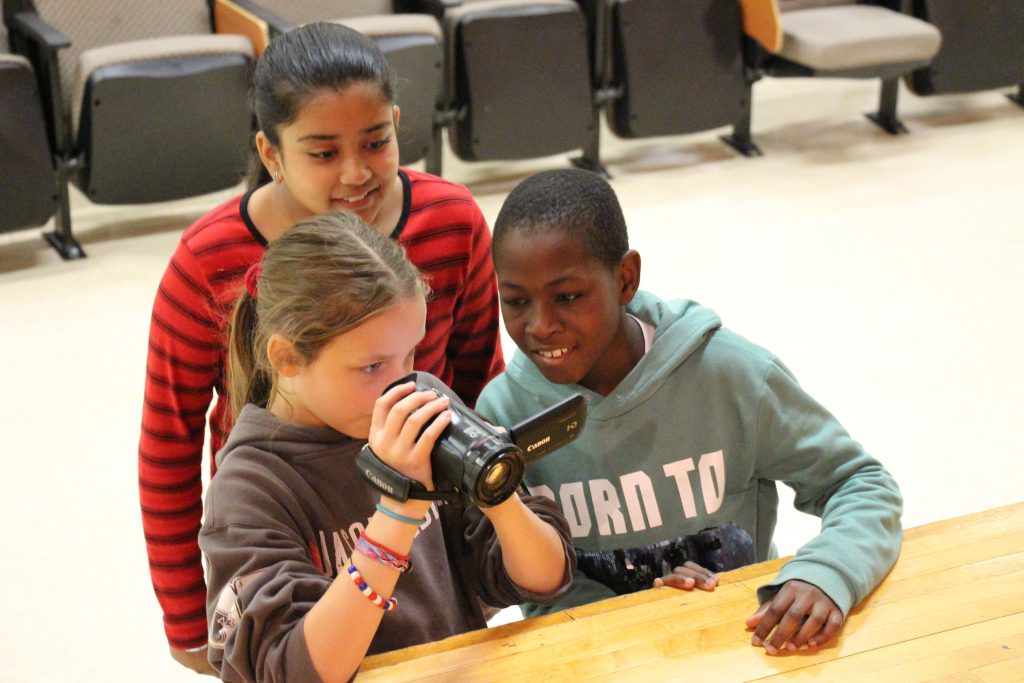 Three students look through the lens of a video camera