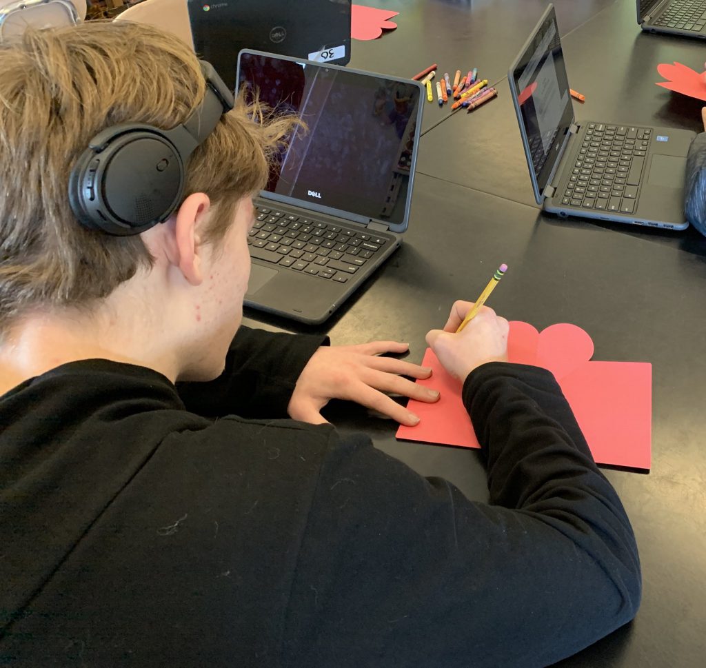 A young man with headphones on his head and wearing a black shirt, draws on a red piece of paper.