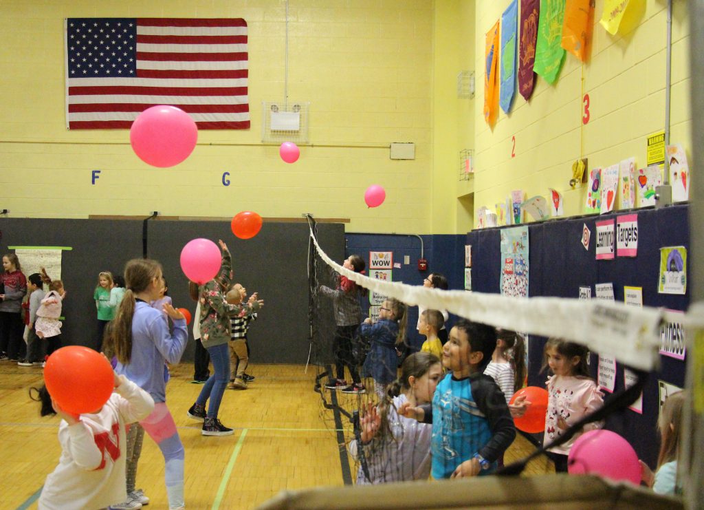 Balloons float in the air above a net as children play balloon volleyball.