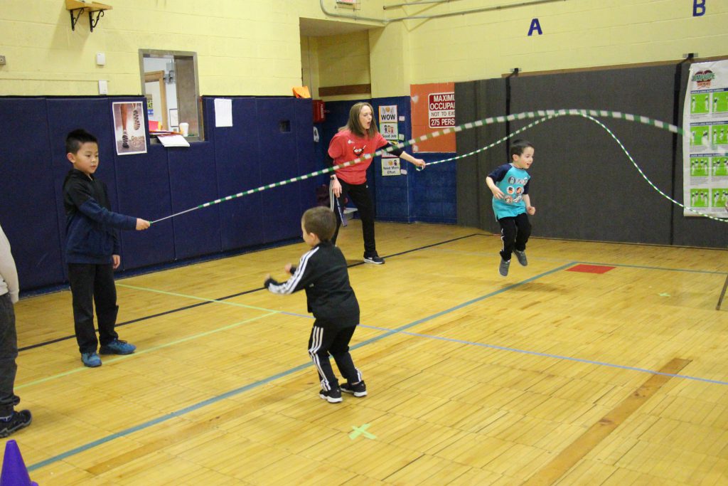 Two small boys jump rope as a young man and a teacher turn the rope for them.