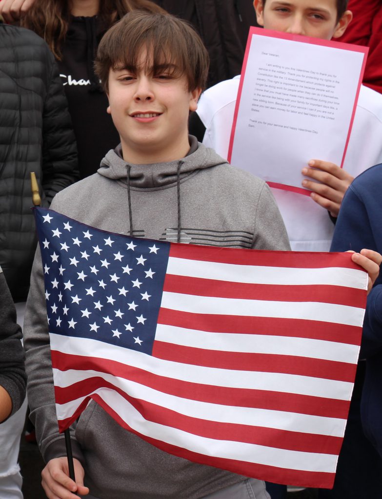 A middle school boy holds an American flag and smiles