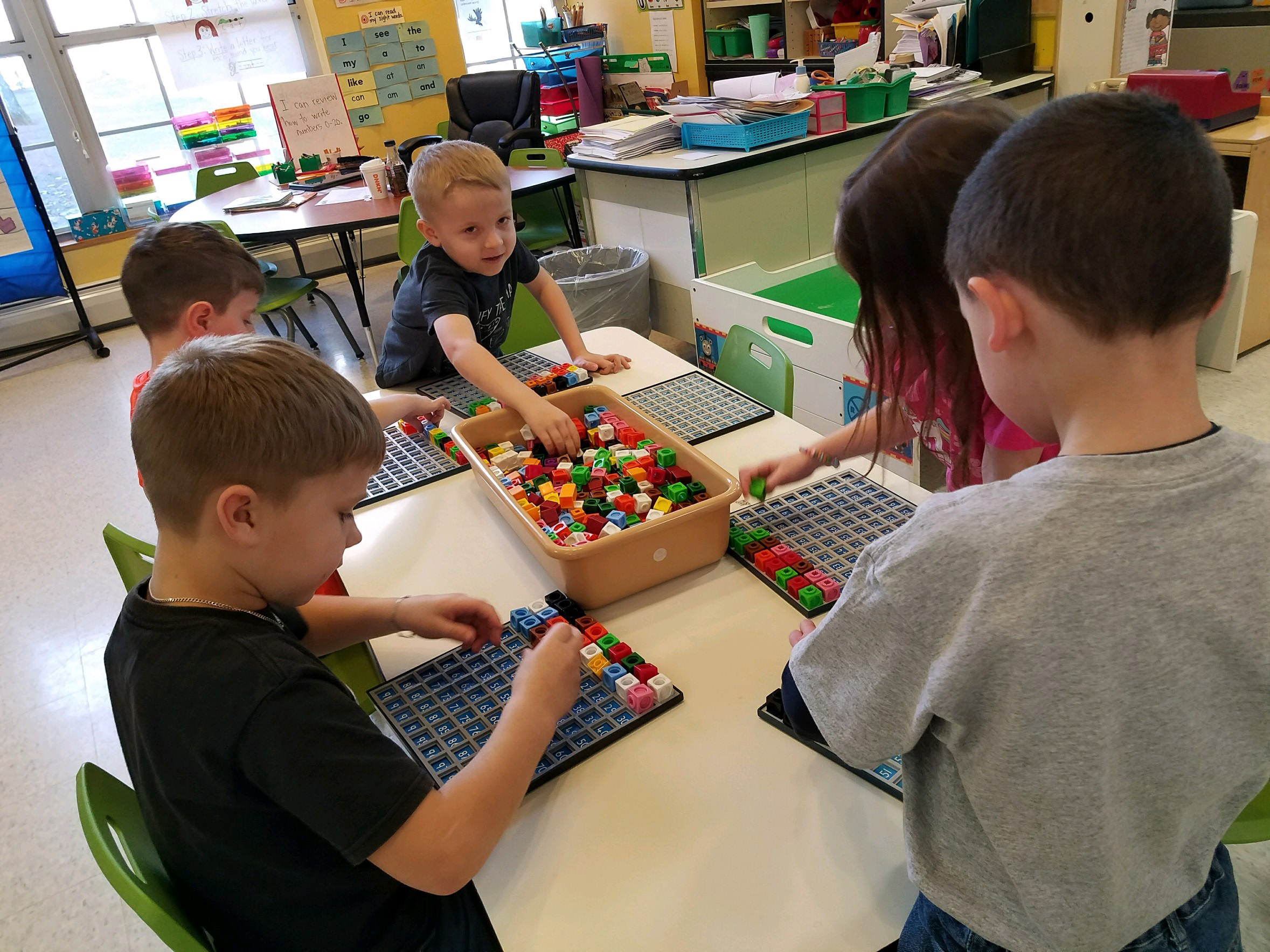 A group of kindergarten students choose colorful blocks to put on their grid which holds 100