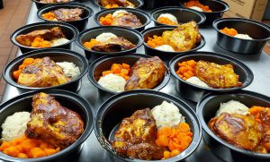 many black containers with chicken, mashed potatoes and carrots in each