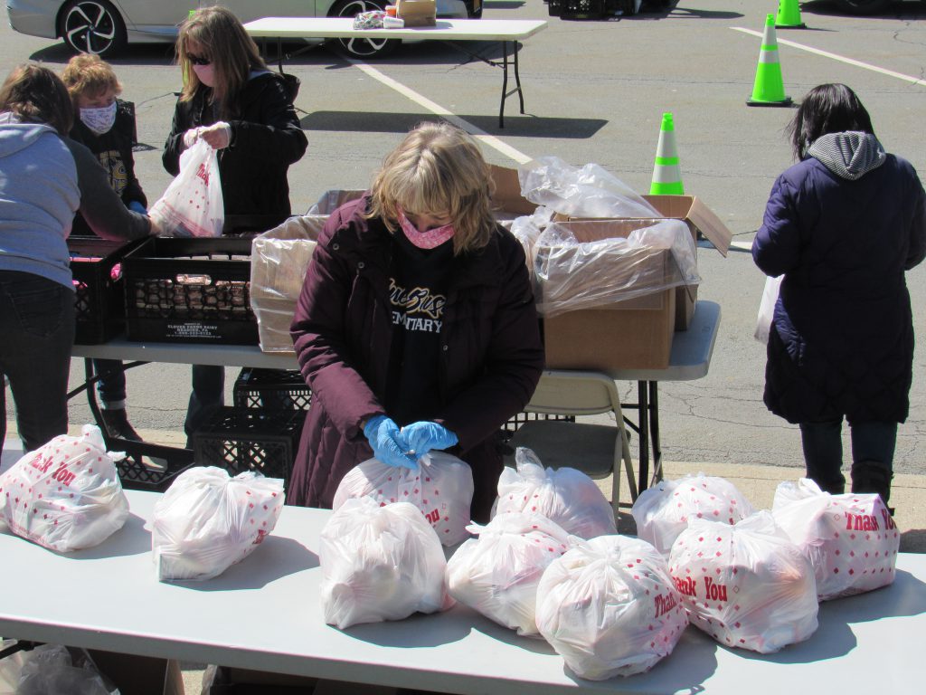 A woman wearing gloves and a face mask packs a white plastic bag with food