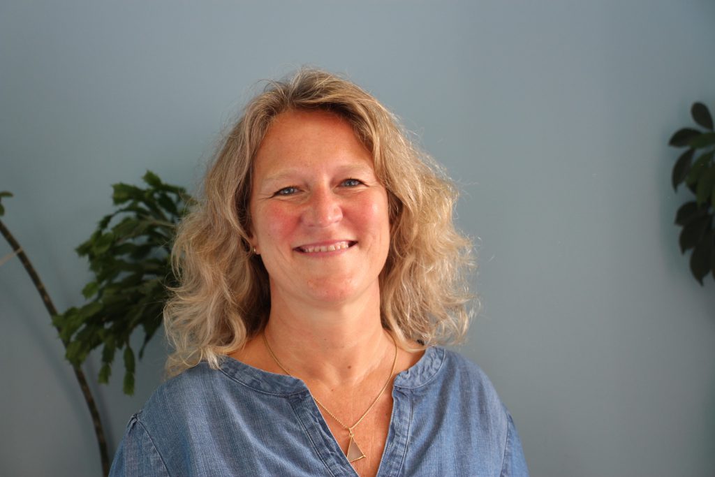 A woman with shoulder length blond hair wearing a blue shirt smiles