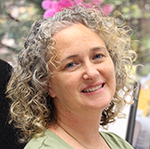 A woman with curly light hair and wearing a green shirt smiles