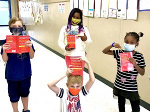 Four third grade students hold their red dictionaries. All are wearing masks.
