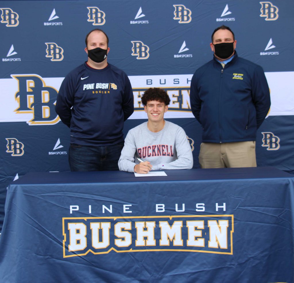 Two men with masks stand behind a young man wearing a gray shirt that says Bucknell