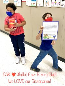 Two third-grade boys wearing masks. One holds up a red dictionary and the other a letter written to the rotary.