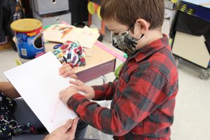 A boy in a black and red checked shirt uses a strawberry to draw